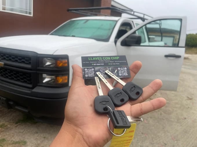 Hand holding car keys with chip in front of white pickup truck