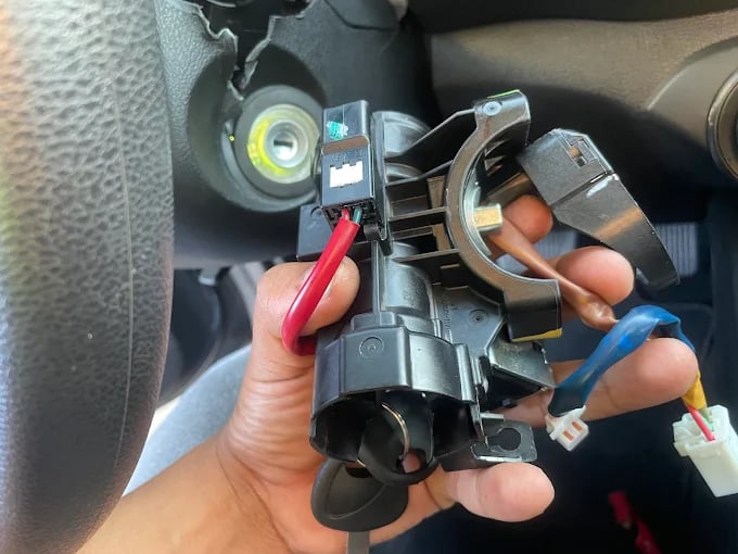 Hand removing ignition switch with colorful wires in car dashboard