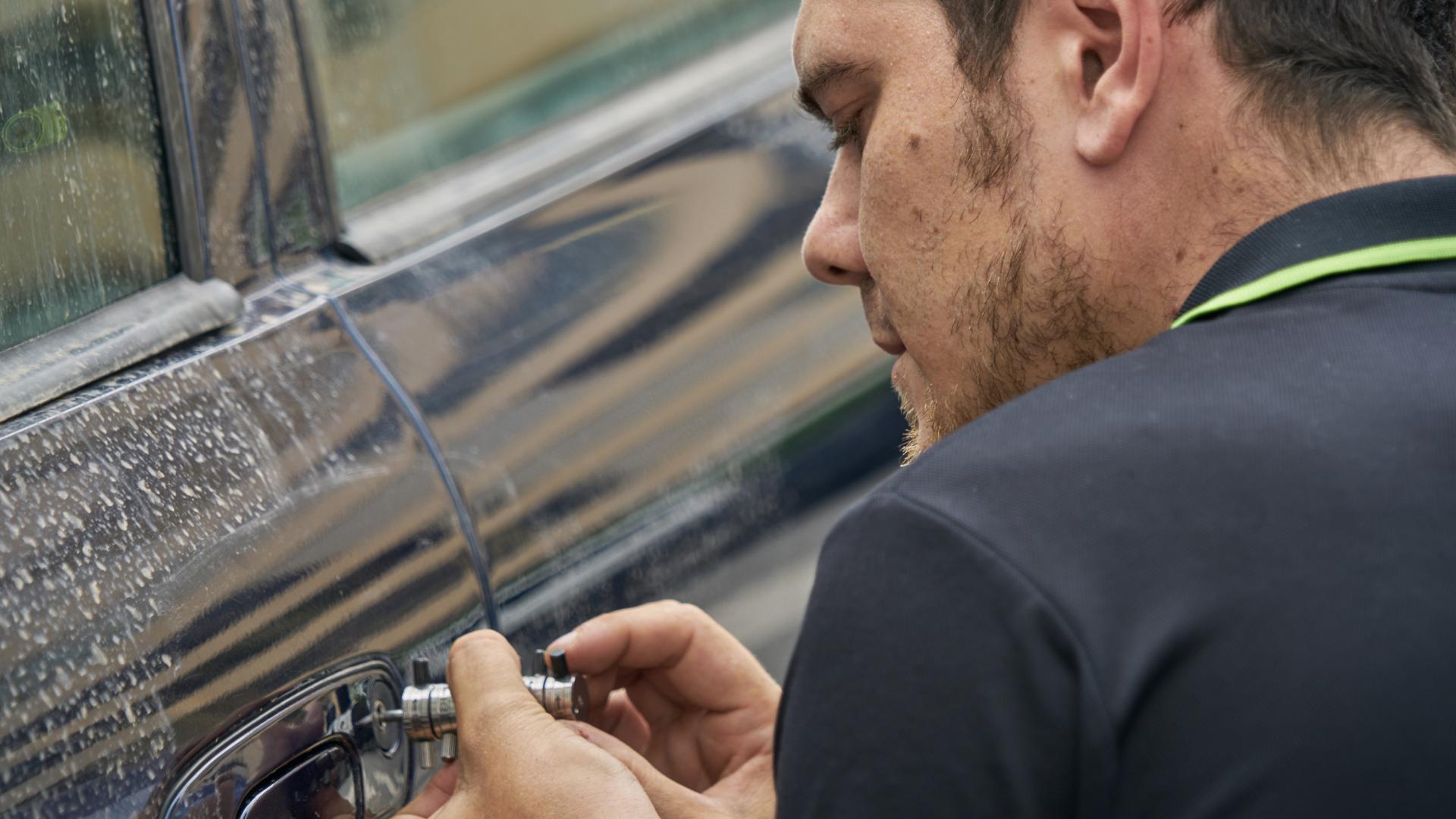 Mobile locksmith technician working on a vehicle door outdoors